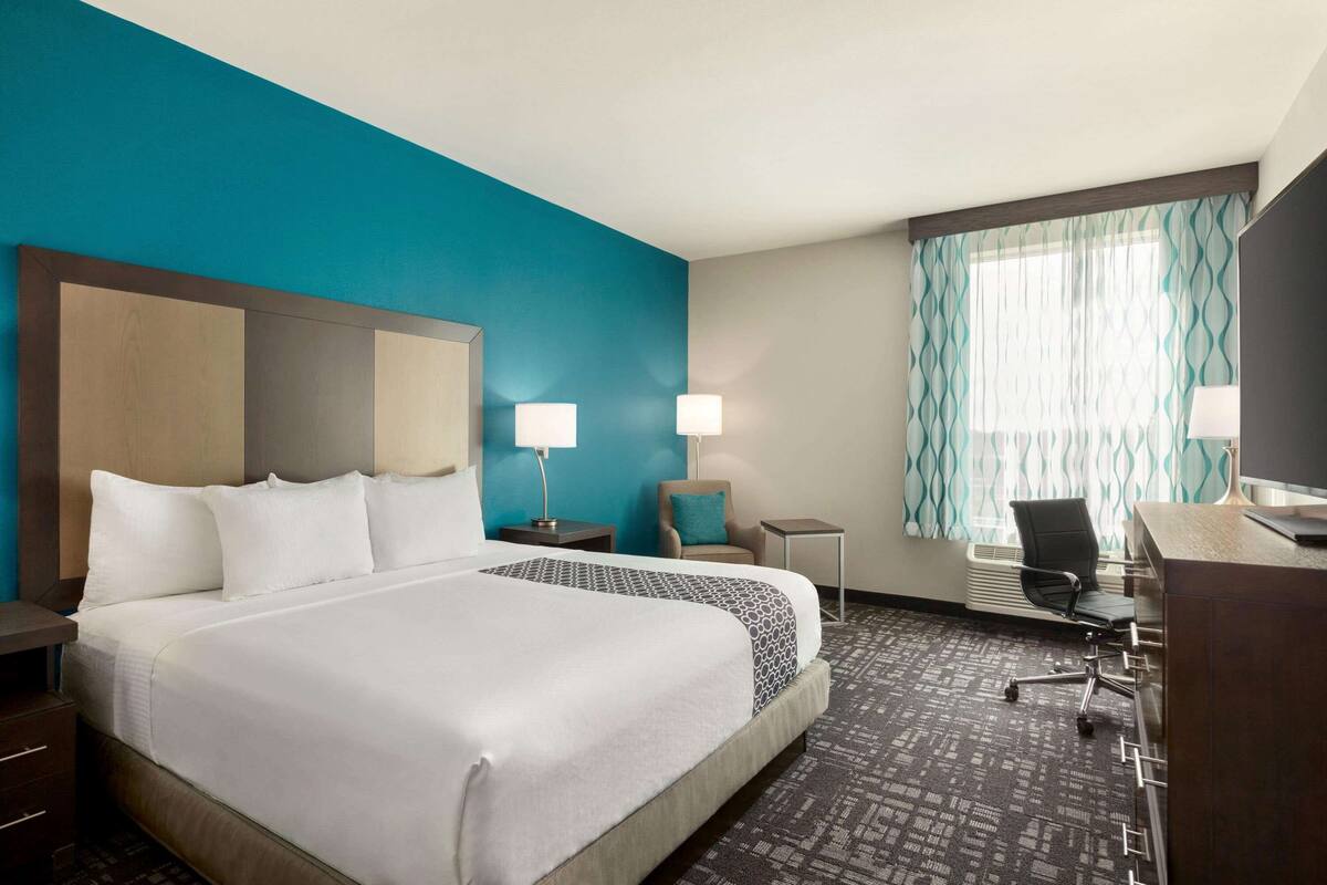 A hotel room with a large bed, a desk, a chair, a lamp, and a window with curtains.