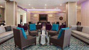 Un vestíbulo de hotel con una zona de estar que incluye sofás y sillones, una mesa de centro y un televisor de pantalla plana montado en la pared.