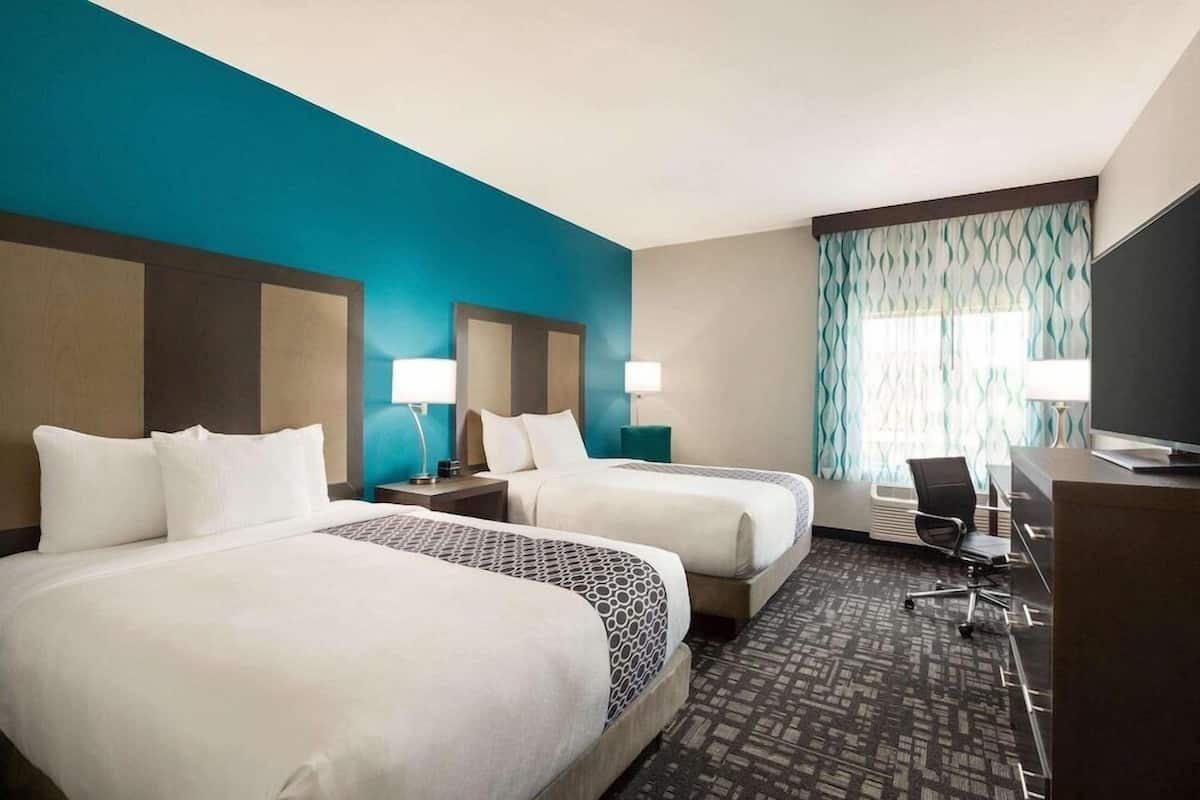 Une chambre d’hôtel avec deux lits, un bureau, une chaise et un téléviseur.