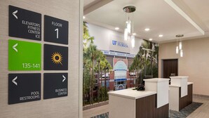 Zona de recepción de hotel con carteles indicativos para ascensores, primer piso, baños de la piscina y centro de negocios.