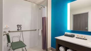 A bathroom with a shower, a wheelchair, a towel rack, and a sink with toiletries.