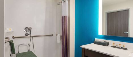 A bathroom with a shower, a wheelchair, a towel rack, and a sink with toiletries.