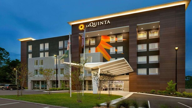 Un hotel moderno con un llamativo letrero de 'La Quinta', un acceso cubierto y un área exterior bien cuidada con estacionamiento.