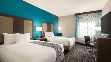A hotel room with two beds, a desk, a chair, and a TV.