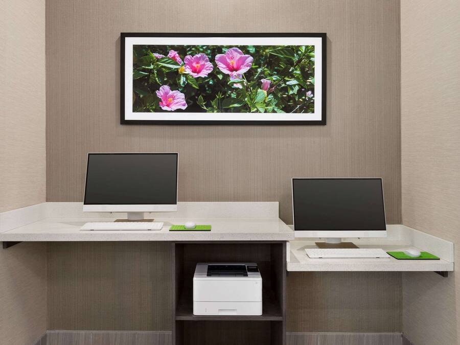 Un bureau moderne, équipé de deux écrans, d’une imprimante et orné d’un tableau représentant des fleurs roses.