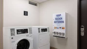 A laundry room with two front-loading washing machines and a wall-mounted soap, bleach, and softener dispenser.