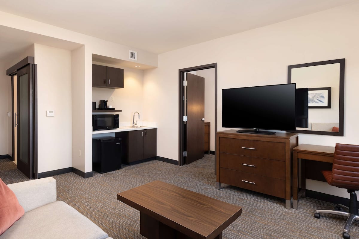 A hotel room with a kitchenette, a flat-screen TV, a desk, and a sofa.