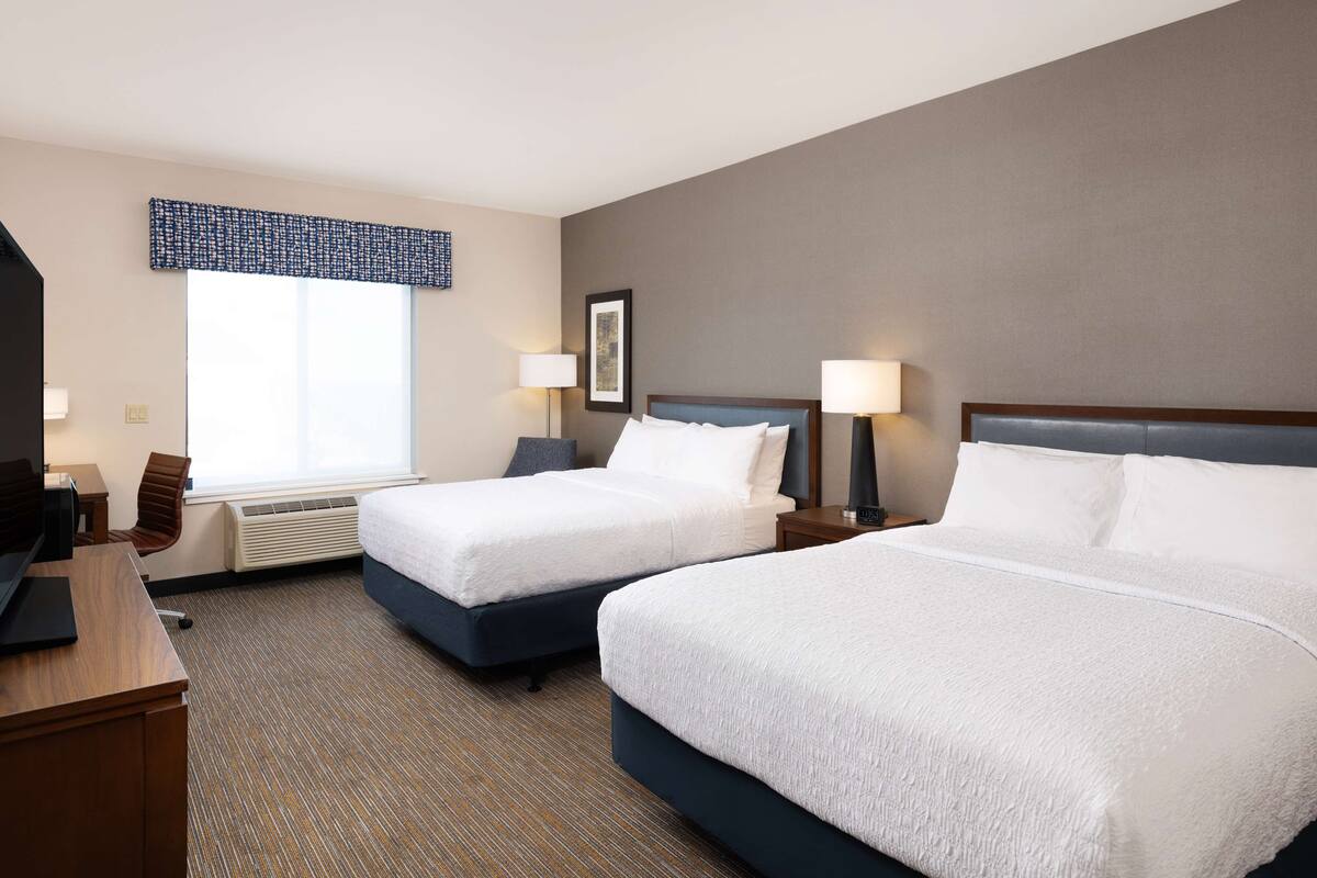A hotel room with two beds, a desk, and a chair.