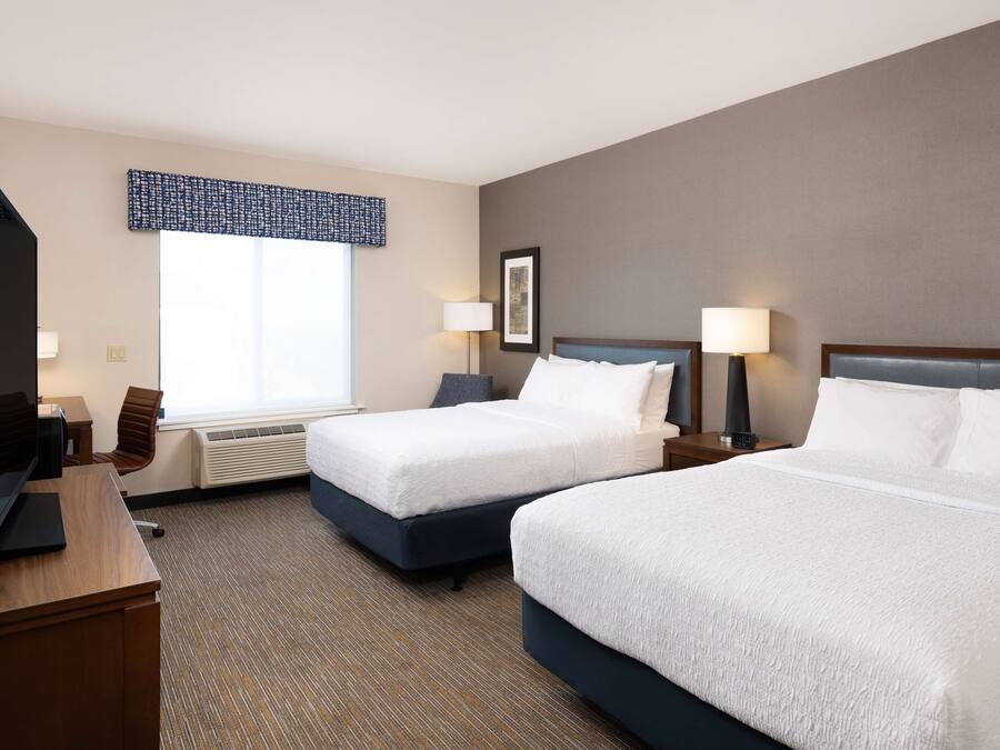 A hotel room with two beds, a desk, and a chair.