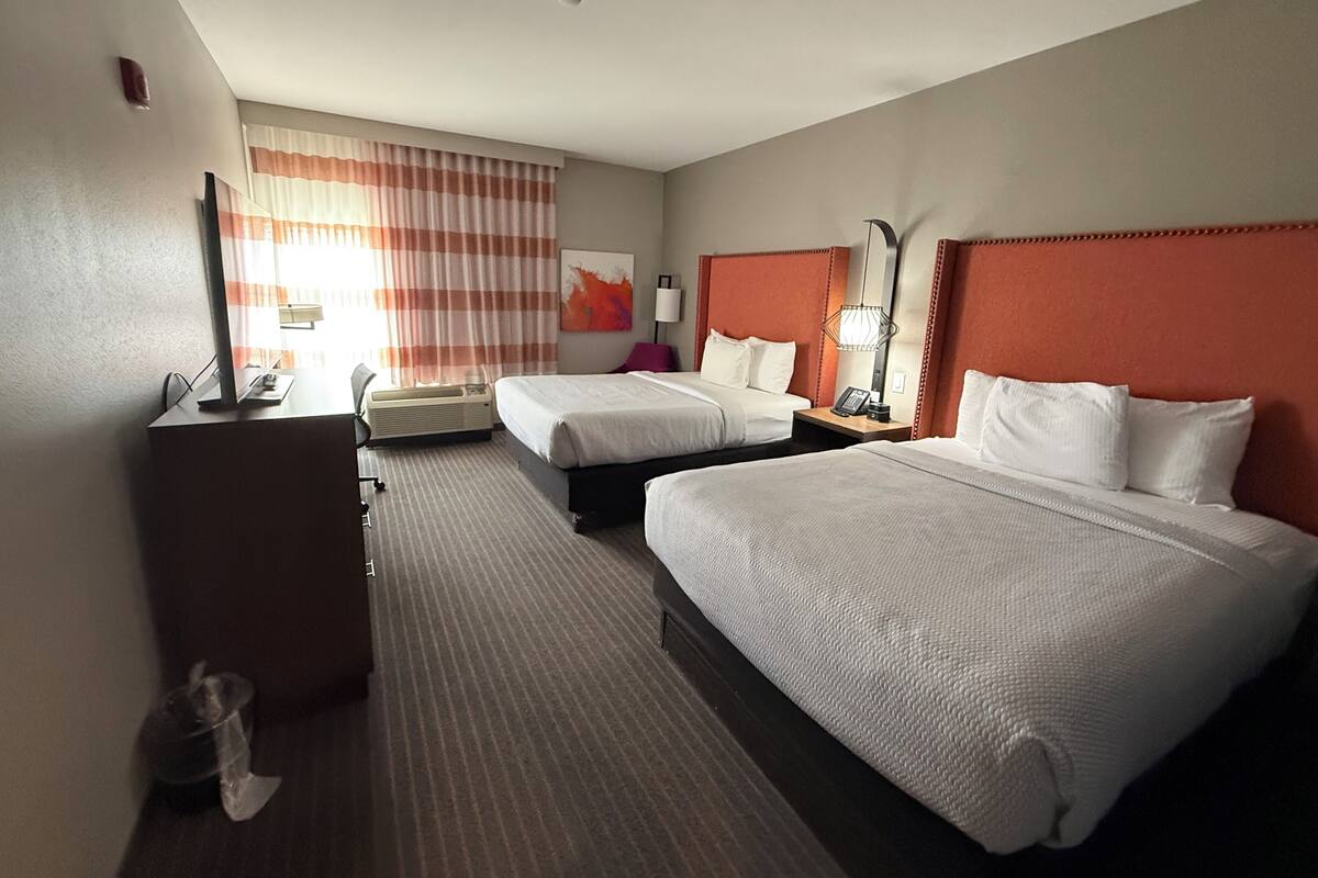 Een hotelkamer met twee bedden, een bureau, een stoel, een lamp en een raam met gordijnen.