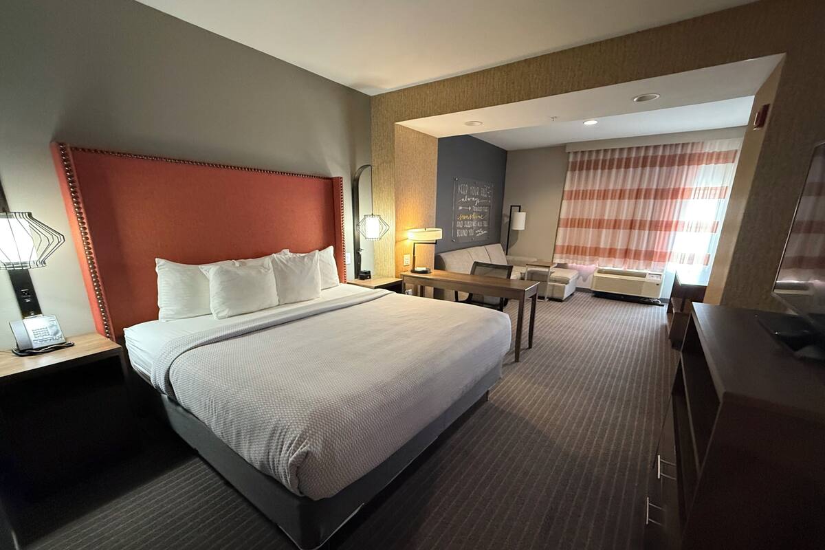 Hotelkamer met groot bed, nachtkastjes, bureau, stoel, televisie en raam met gordijnen.