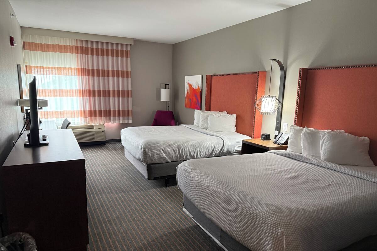 Hotelkamer met twee bedden, een bureau met een computer, een stoel, een lamp en een schilderij aan de muur.