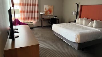 A hotel room with a bed, desk, chair, and a lamp.