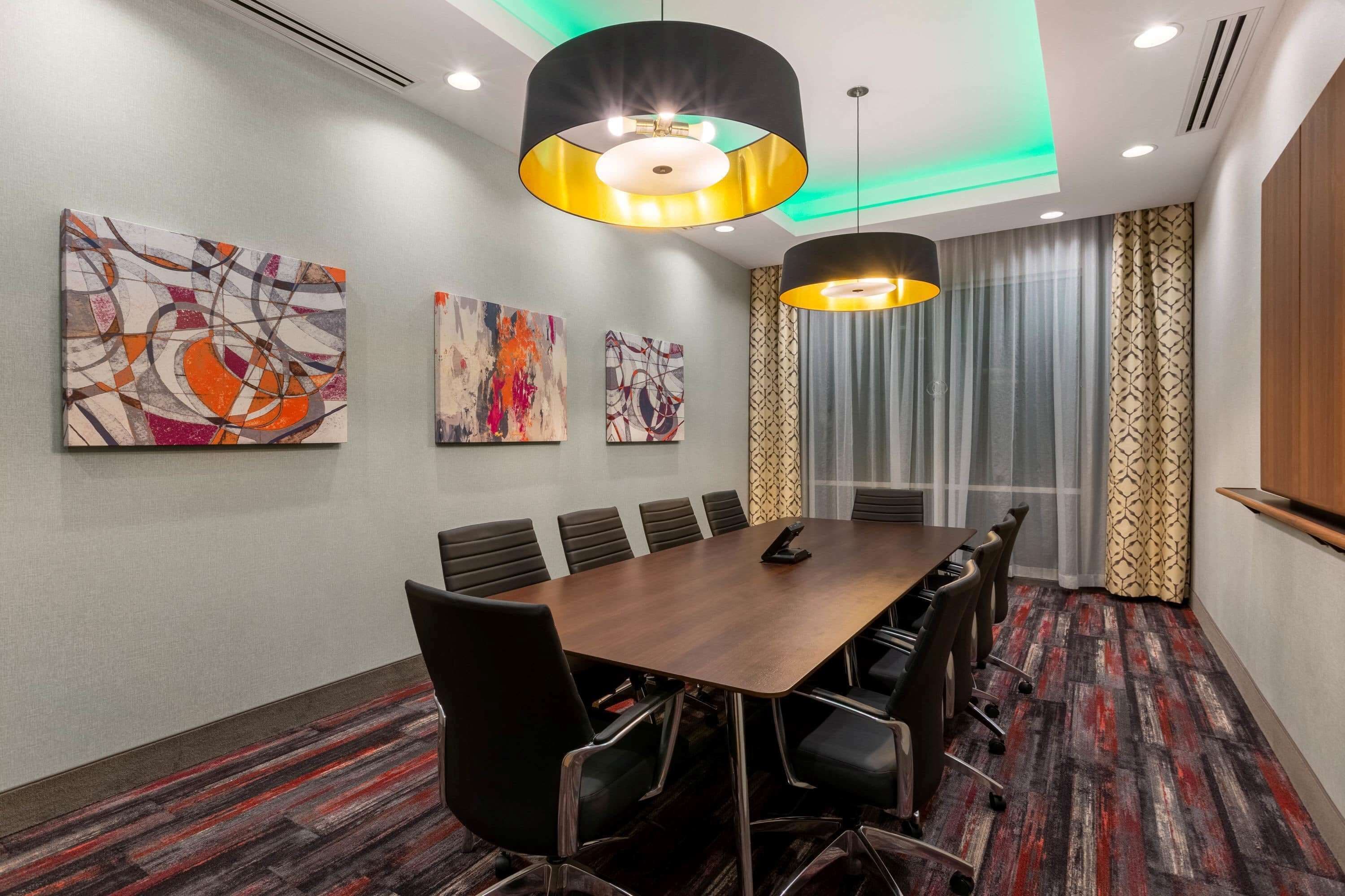A conference room with a long table, chairs, and three abstract paintings on the wall.