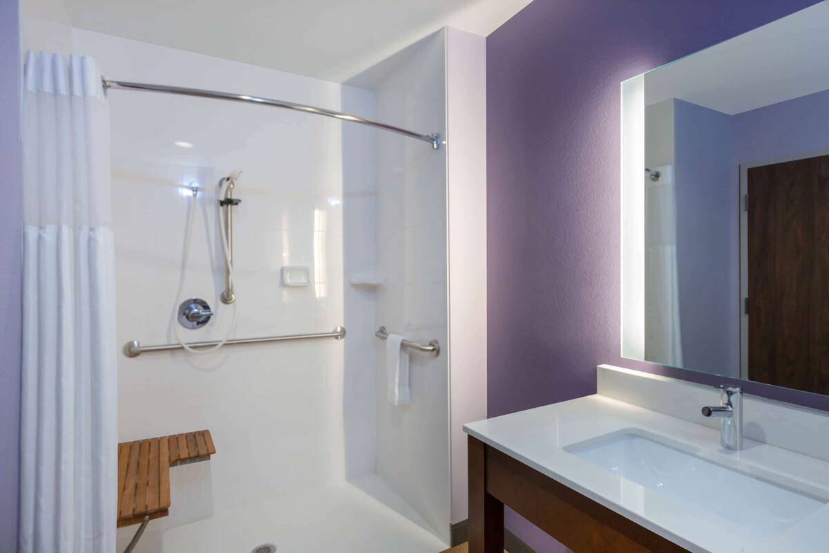 Een moderne badkamer met een douche met glazen wand, een witte wastafel en een grote spiegel.