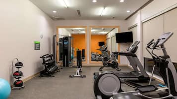 A gym with treadmills, elliptical machines, weight machines, and a blue exercise ball.