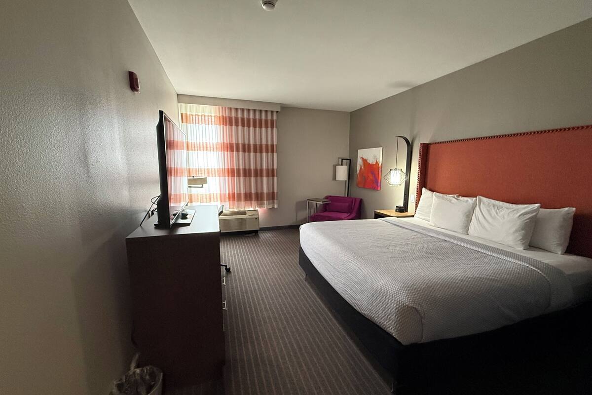Hotelkamer met een bed, bureau, stoel, televisie en een raam met gordijnen.