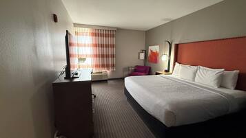 Une chambre d’hôtel avec un lit, un bureau, une chaise, une télévision et une fenêtre avec des rideaux.