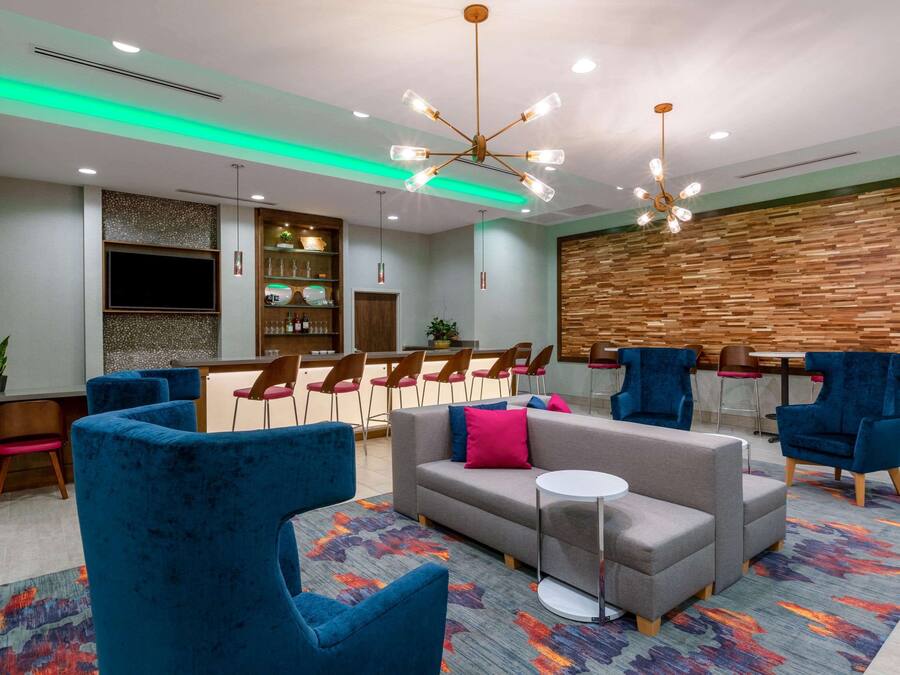 Un espace de détente moderne comprenant un canapé, des fauteuils bleus, une petite table et un panneau mural en bois.