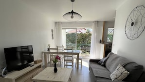 A modern living room with a flat-screen TV, a wooden coffee table, and a grey sofa. - Cambo: Bright T2 with South Terrace, Wifi & Parking (Cambo-les-Bains)