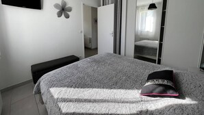 A bedroom with a bed, a bench, a flower wall decoration, a wardrobe, and a hanging light fixture. - Cambo: Bright T2 with South Terrace, Wifi & Parking (Cambo-les-Bains)