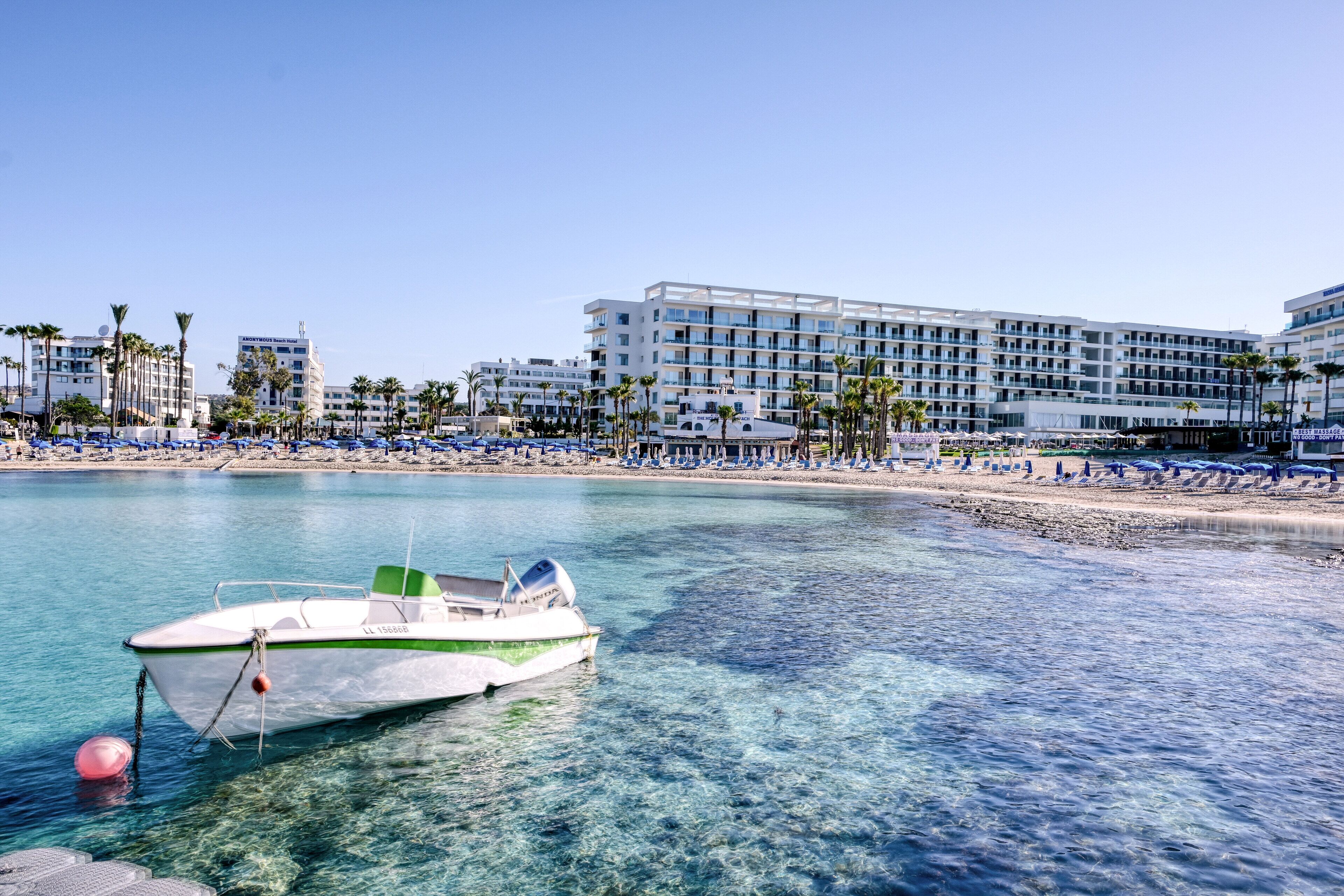 Una marina con un barco atracado cerca de una playa, con un hotel al fondo.