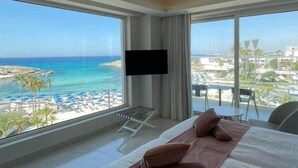 Ein Hotelzimmer mit einem großen Bett, einem Flachbildfernseher und einem Balkon mit Blick auf Strand und Meer.