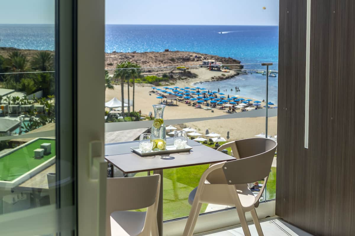 Un balcón con mesa y sillas que da a una playa con sombrillas y una vista despejada del mar.