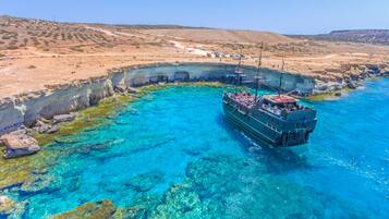A boat anchored near a rocky coastline with clear blue waters.