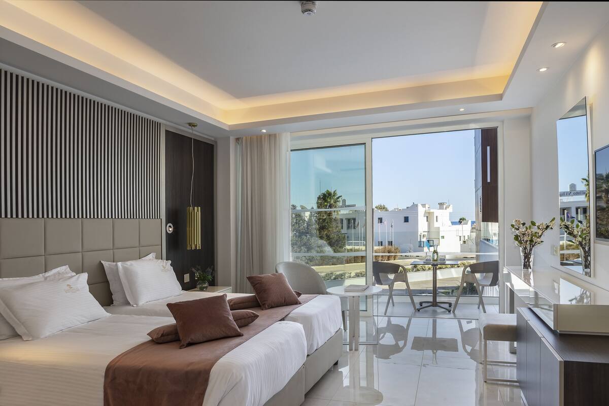 Una habitación de hotel moderna con una cama grande, un escritorio y un balcón con vistas a la ciudad.