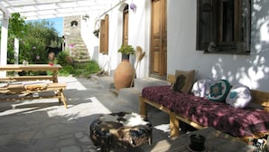 A covered outdoor area with a wooden bench, a table, and a potted plant.