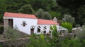 A white building with a red-tiled roof, stone walls, and a white porch.