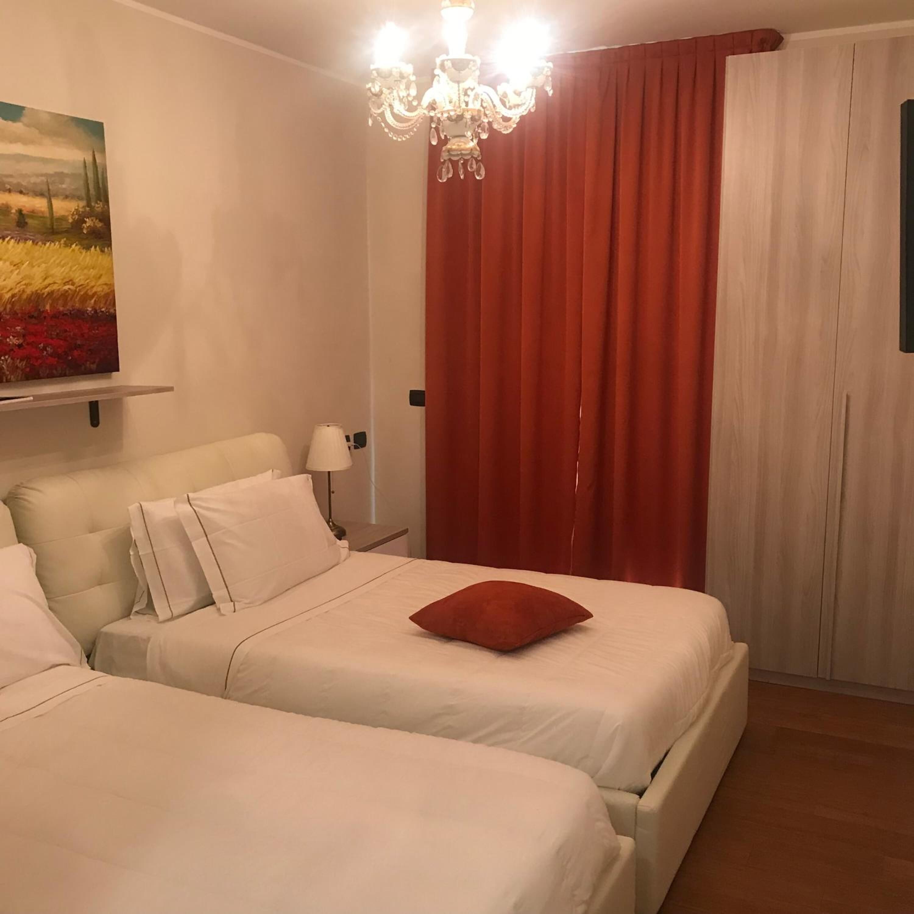 Una habitación de hotel con dos camas, una araña, un cuadro en la pared y una cortina roja.