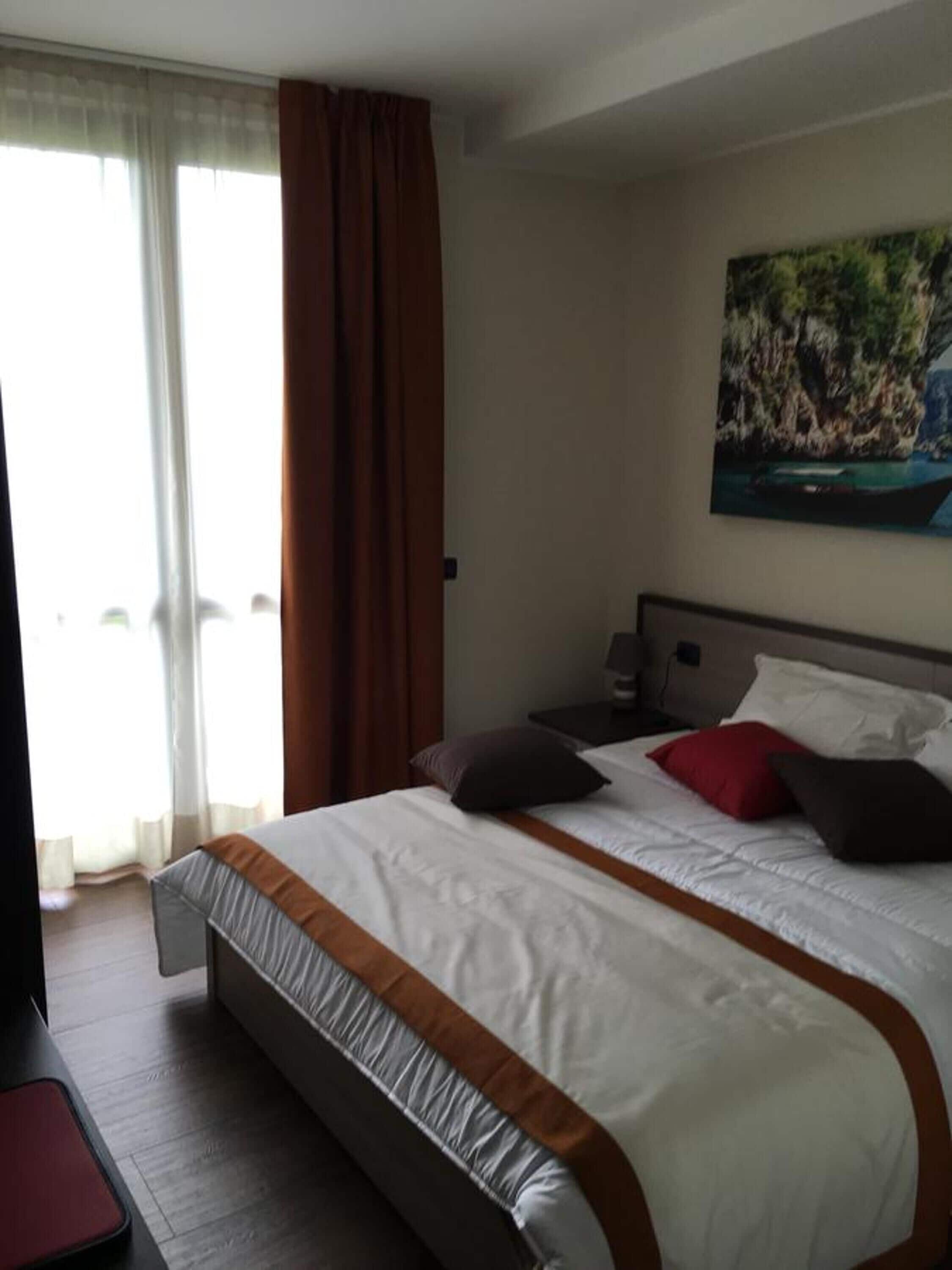 Camera d'hotel con un letto grande, un quadro appeso alla parete e vista sull'esterno dalla finestra.