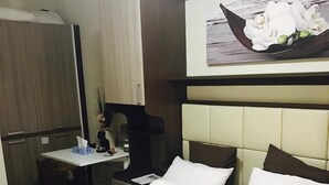 Quarto de hotel com cama, escrivaninha e cadeira. Há um quadro na parede acima da cama.