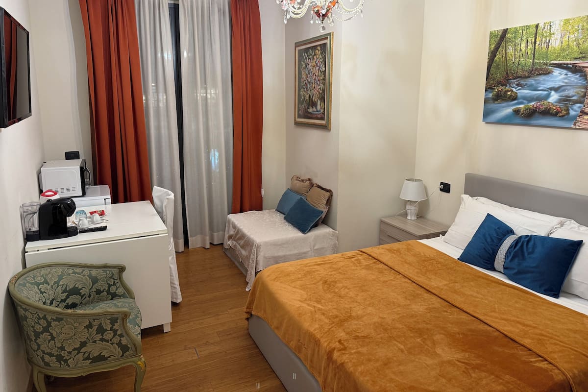 A hotel room with a bed, a desk, a chair, a painting, and a chandelier.