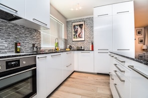 Una cocina moderna con armarios blancos, un salpicadero negro y piso de madera.
