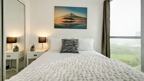 Une chambre d’hôtel avec un grand lit, une table de chevet avec des lampes, un tableau représentant une montagne et une vue sur un parc par la fenêtre.