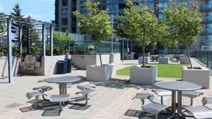 Un espace extérieur aménagé en terrasse, dot é de plusieurs coins salon, notamment des tables et des bancs, et entouré de jardinières et d’arbres.