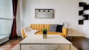 Un salon moderne avec un canapé, une table basse, une petite table d’appoint et une plante en pot.