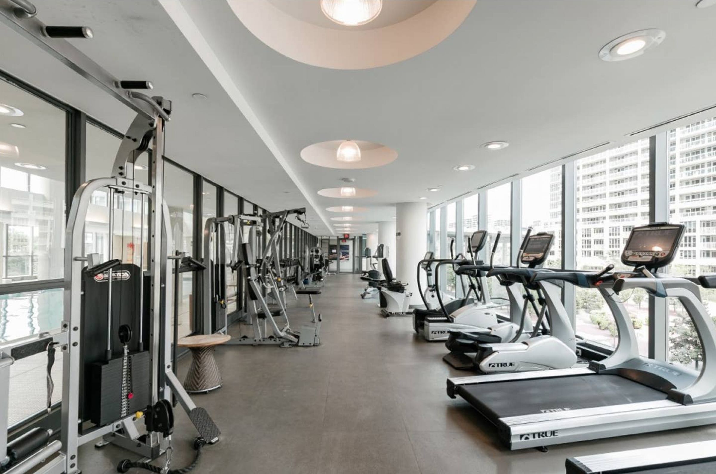 Un gimnasio con máquinas de cardio y equipo de pesas, amplias ventanas y un diseño de techo moderno.