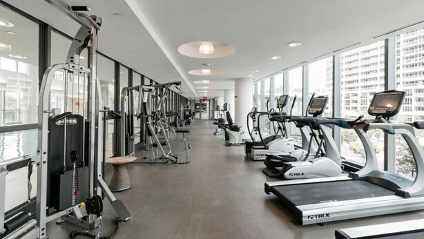 Une salle de sport équipée de machines de cardio et de matériel de musculation, dotée de grandes fenêtres et d’un design moderne au niveau du plafond.