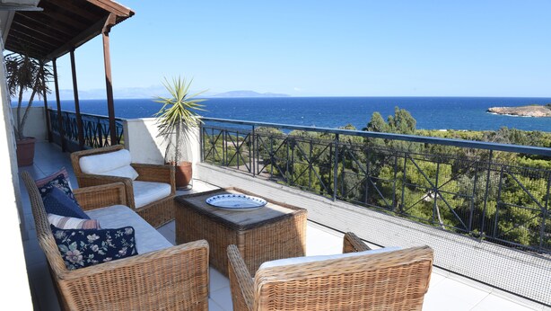 Un balcón con mobiliario de mimbre, una planta en maceta y vistas al mar.
