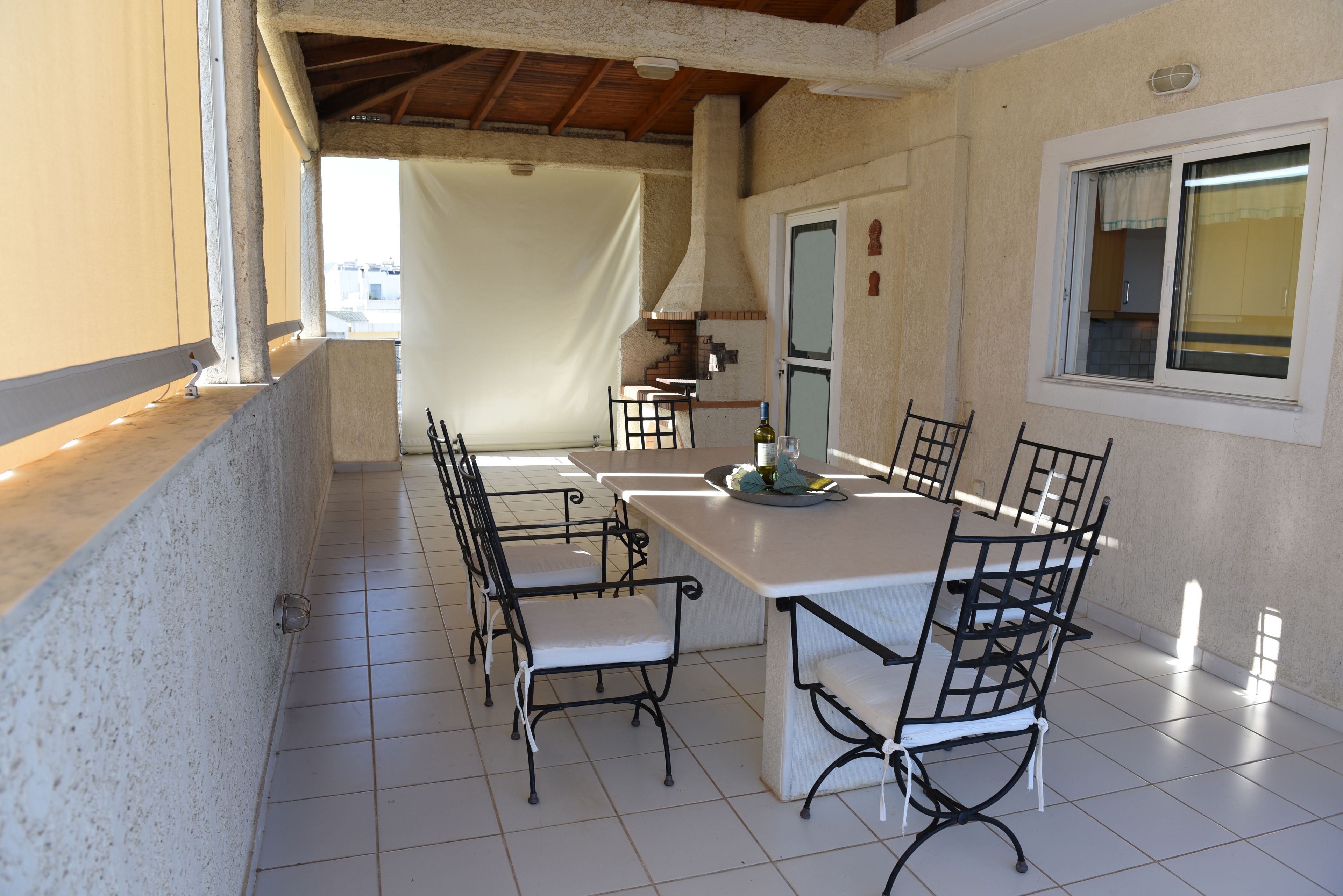 Un coin repas avec une table blanche et des chaises en métal noir, un sol carrelé et une fenêtre donnant sur un paysage agréable.