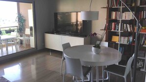 Una zona de menjador moderna amb una taula rodona i cadires, una estanteria i una televisió.