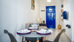 A dining area with a round table set for four, a blue door in the background, and a clock on the wall. - Apartment Tsilivi Blue Vista (Zakynthos)