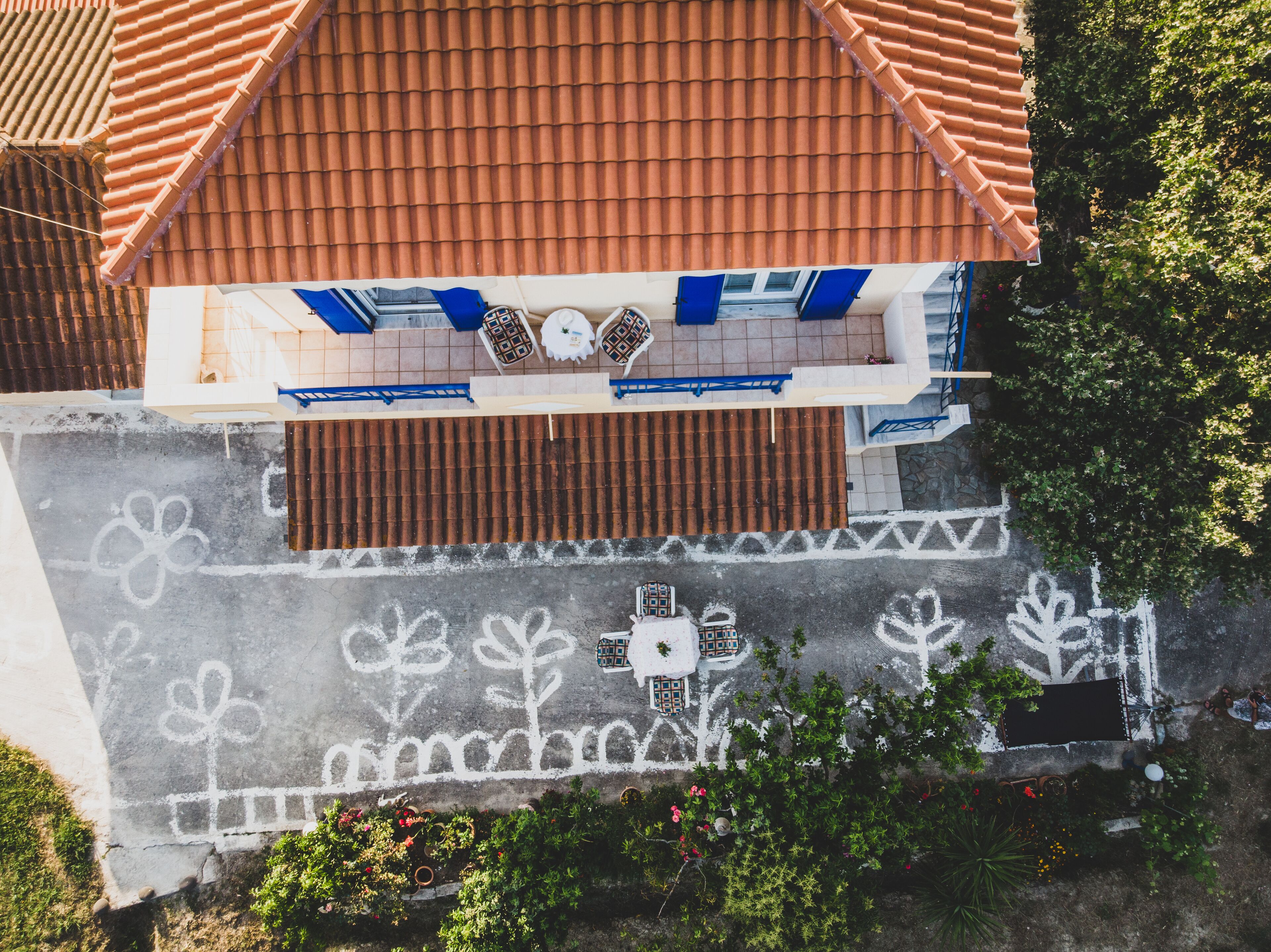 An aerial view of a building with a tiled roof, a balcony with blue railings, and a courtyard with a patterned pavement.