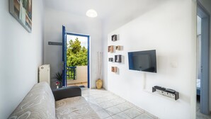 A modern living room with a sofa, a flat-screen TV mounted on the wall, and a small shelf with remote controls. - Apartment Tsilivi Blue Vista (Zakynthos)