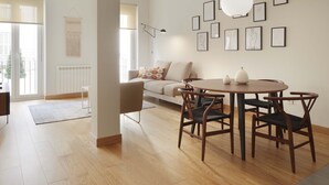 Ein modernes Wohnzimmer mit Holzboden, einem runden Esstisch mit Stühlen, einer Couch mit Kissen und einer Wand mit gerahmten Kunstwerken.