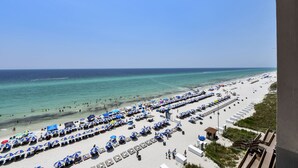 A beach with rows of umbrellas and sun loungers, a clear sky, and the ocean.